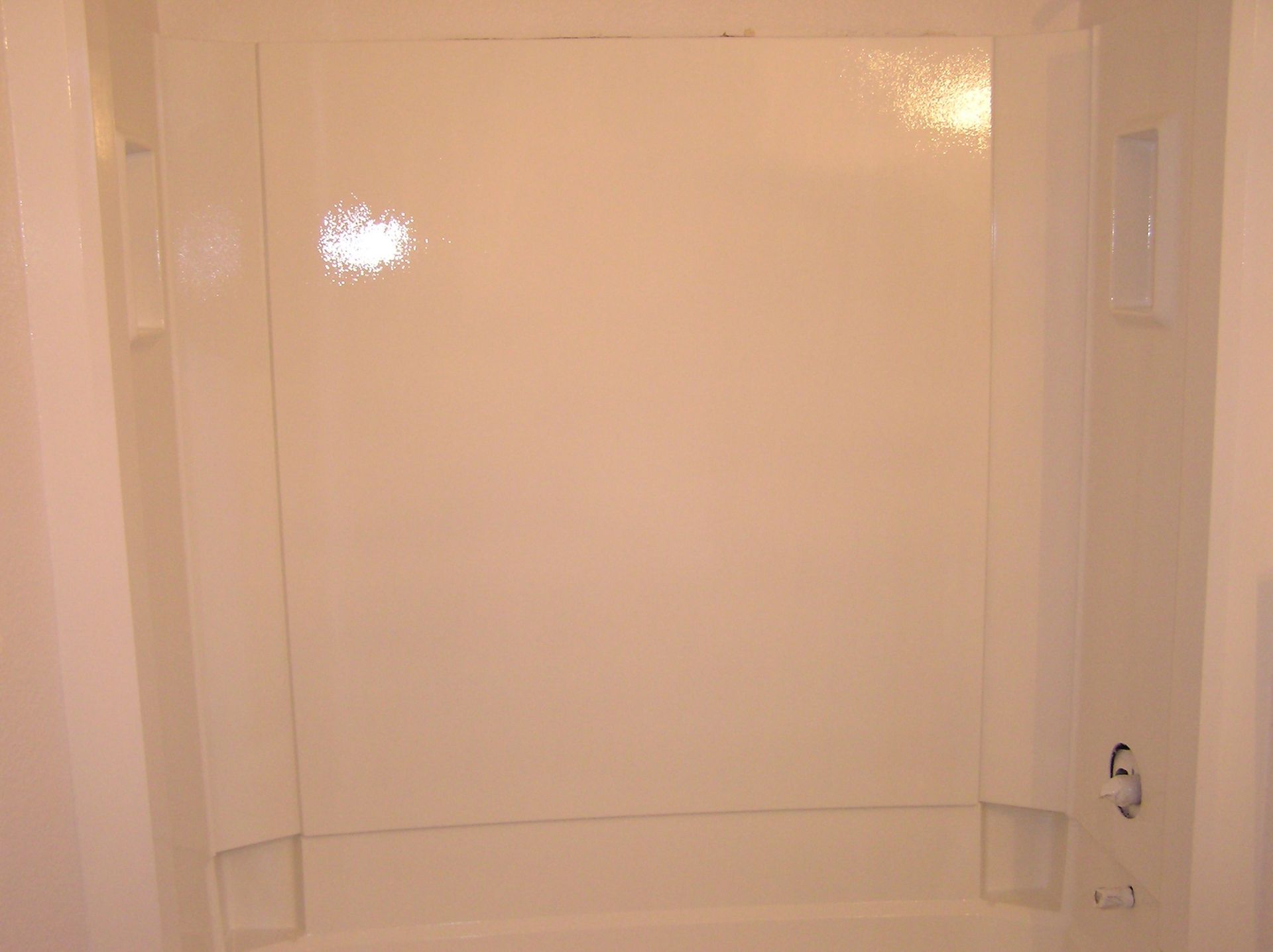 White, empty shower stall with built-in soap dishes and faucet.