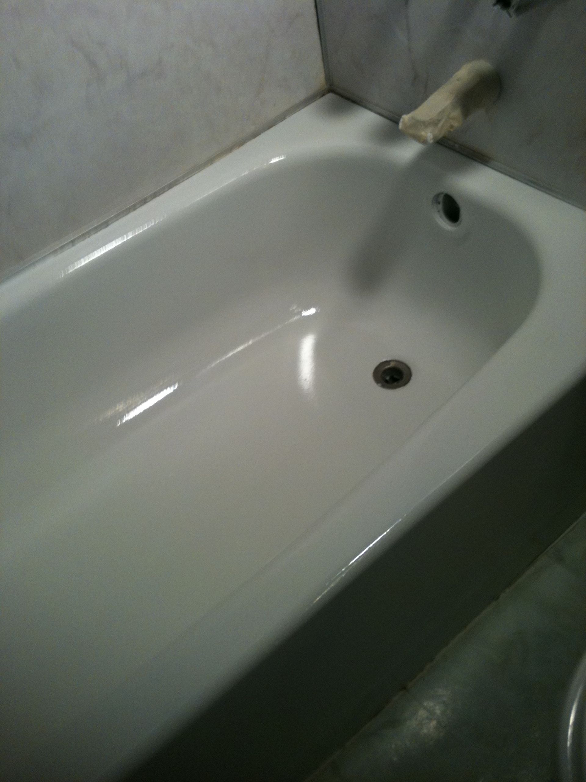 White bathtub with overflow drain and drain, against a tiled wall.