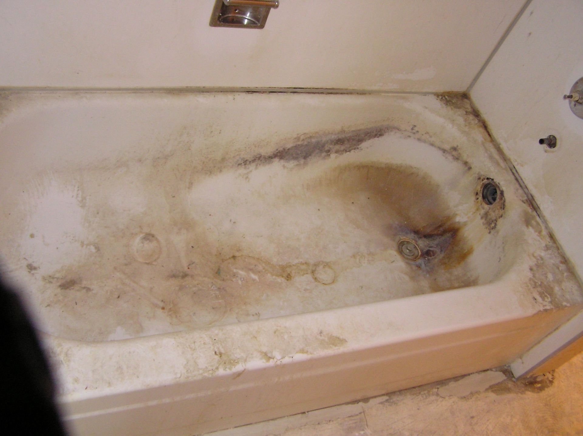Dirty, stained white bathtub with dark brown and black discoloration.