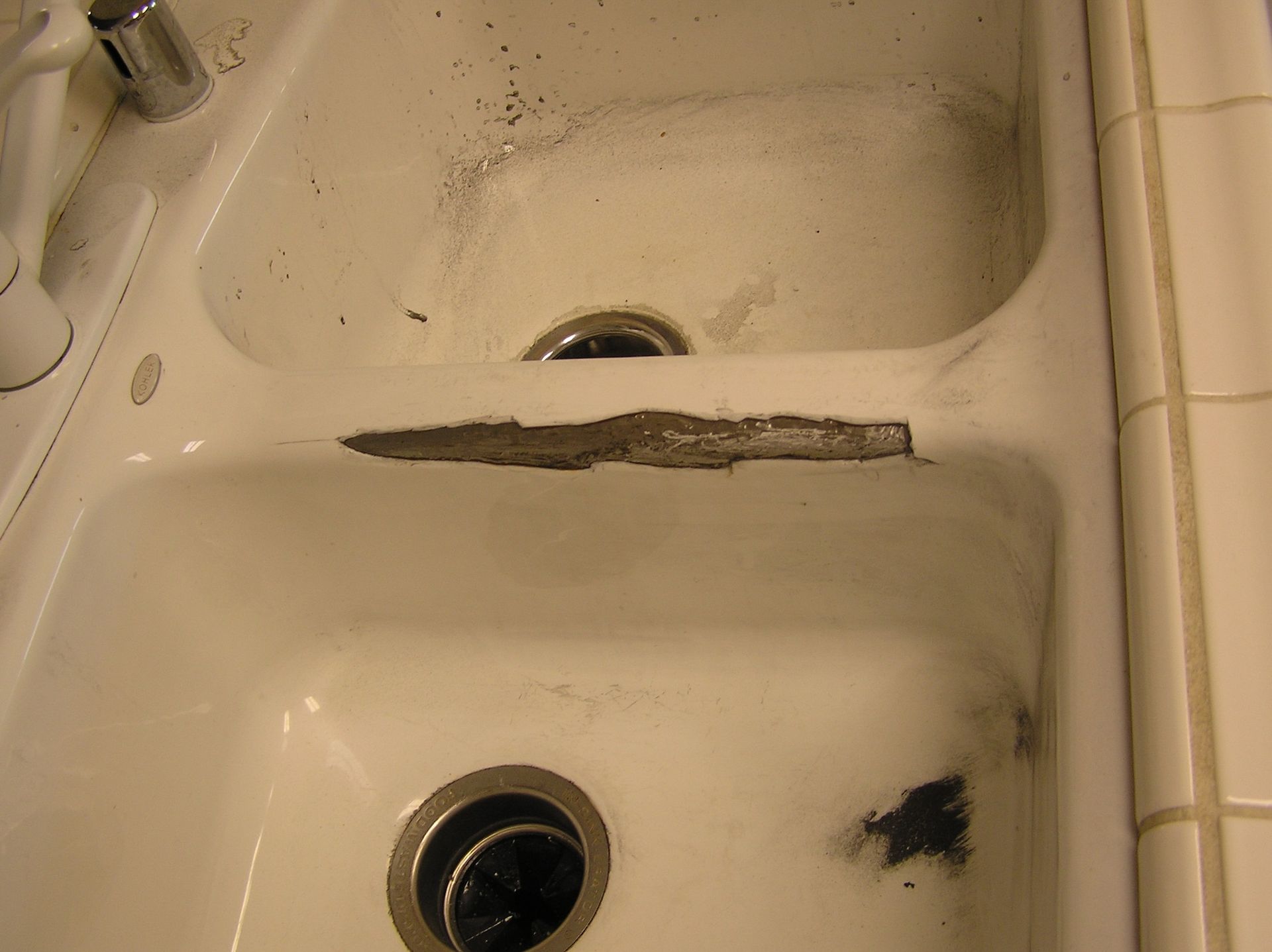 A white porcelain double sink with damage between the basins and debris.