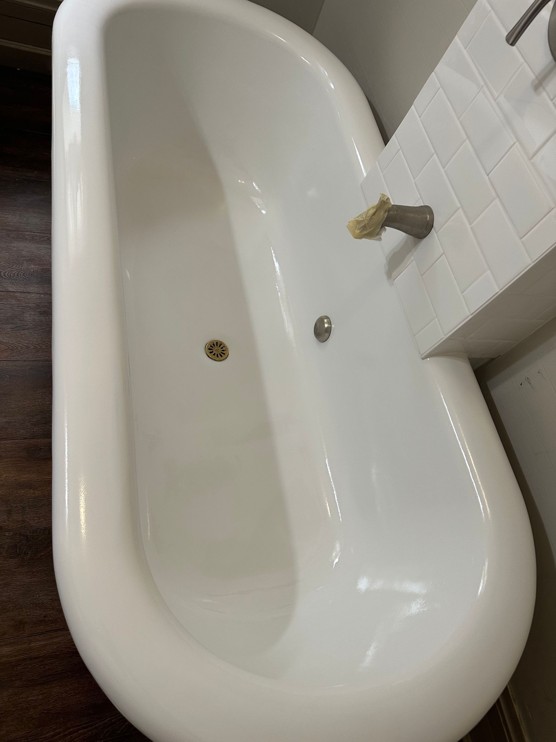 White bathtub with gold fixtures, set against a tiled wall and dark wood flooring.