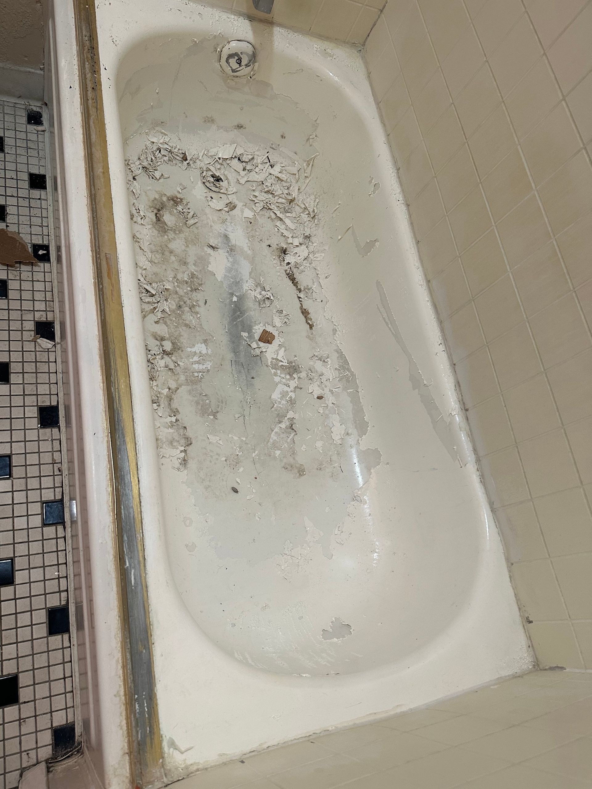 Dirty, worn white bathtub. Brown debris and mildew in the bottom. Tile floor and walls.