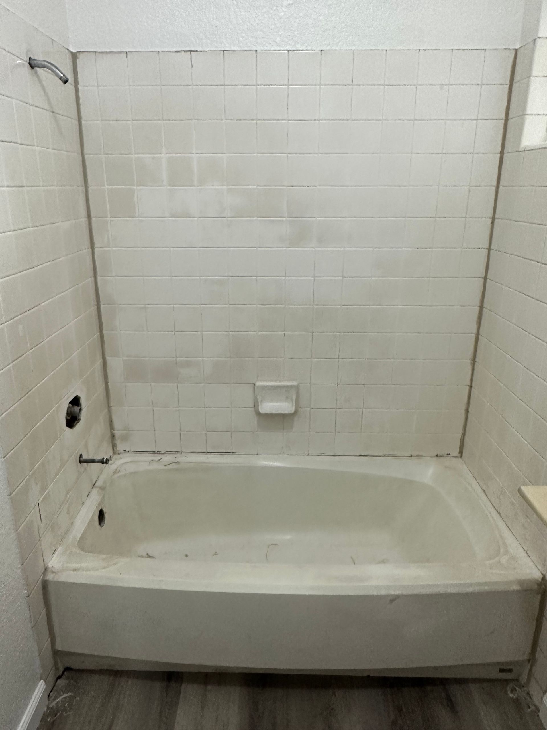 White bathtub and tiled shower surround in a bathroom with dark flooring.