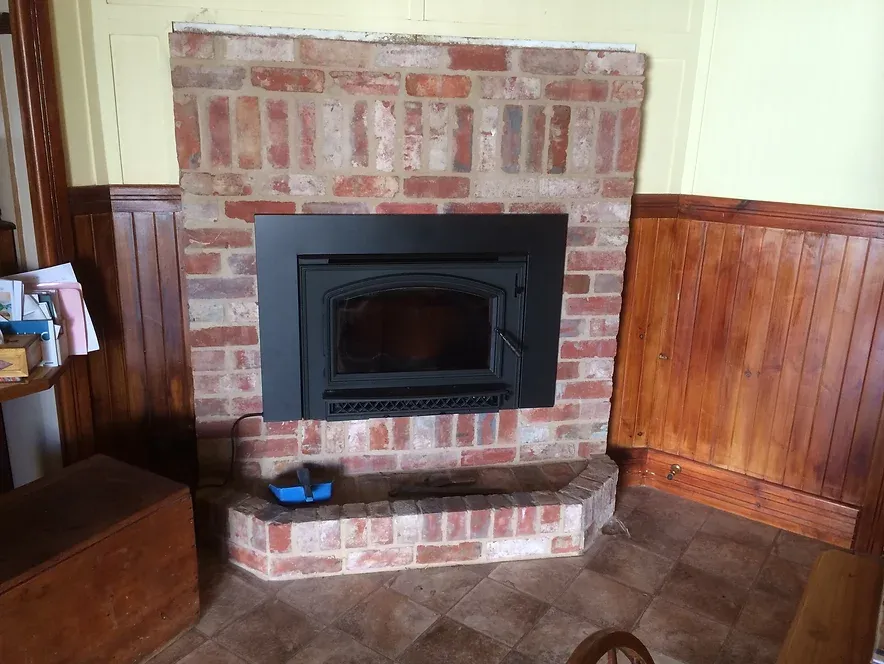 a brick fireplace made by dwr services with a wood stove in a living room .