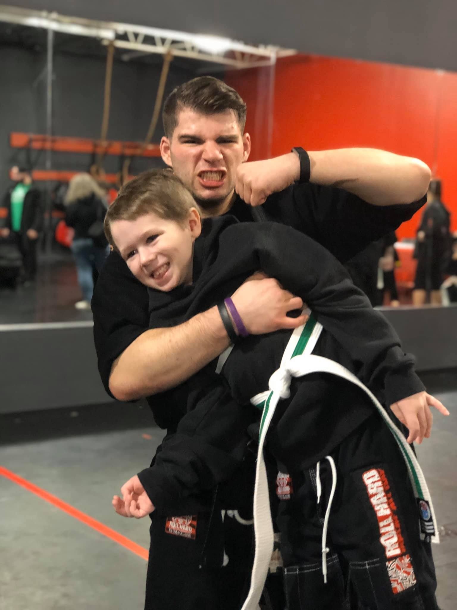 a man is holding a young boy who is wearing a black sweatshirt that says full guard