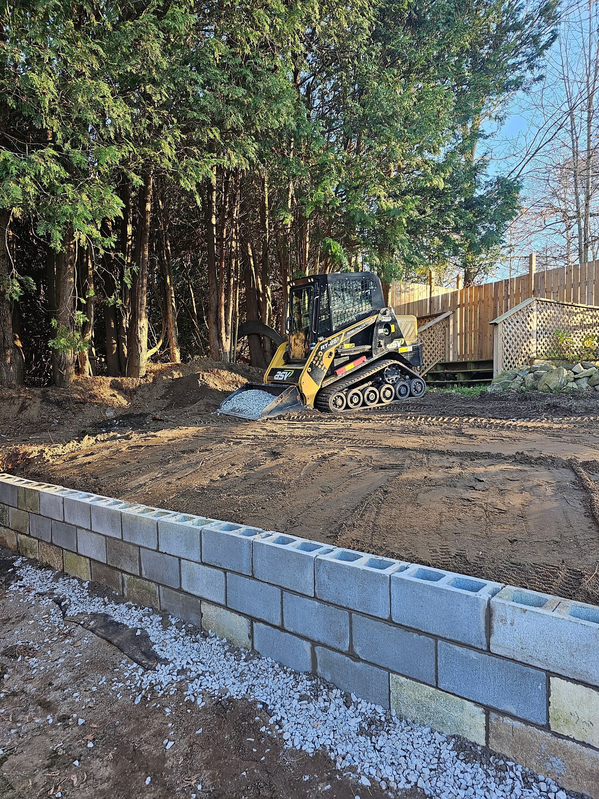 a bulldozer is working on a dirt field next to a brick wall .