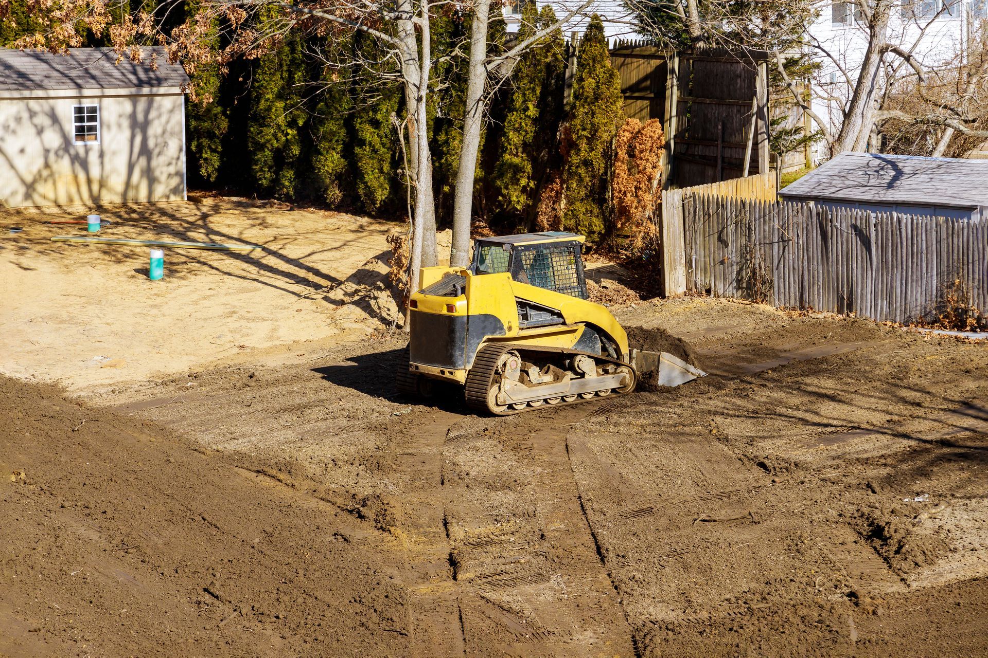 a yellow bulldozer is moving dirt in a backyard .