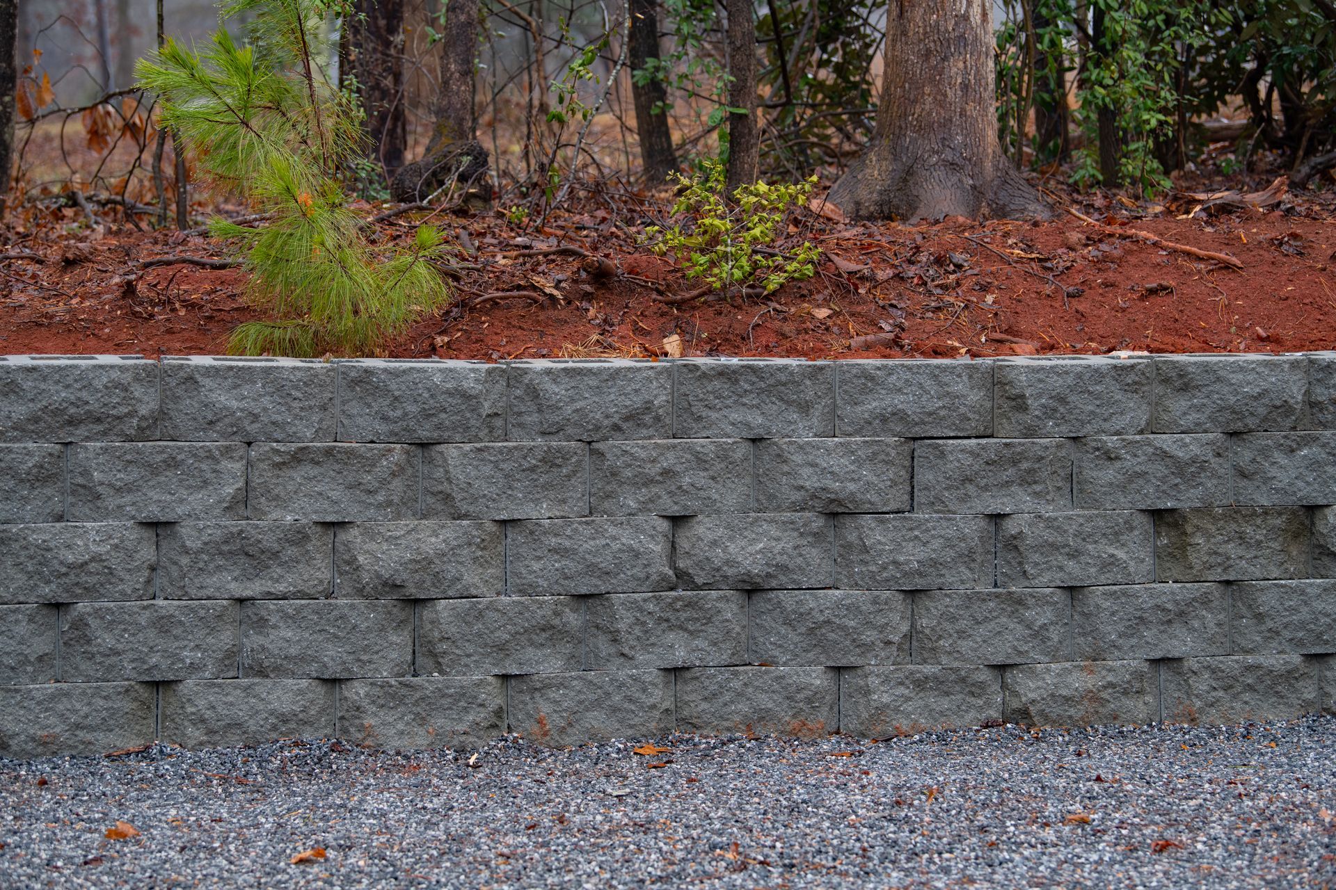 a brick wall is surrounded by gravel and trees in the background .