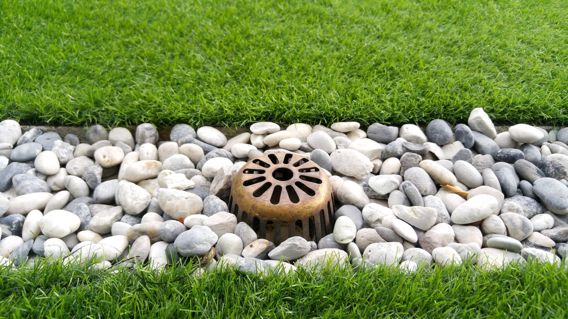 a drain hole in the grass surrounded by rocks .