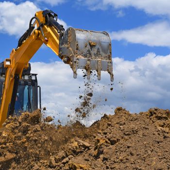 a yellow excavator is digging a pile of dirt