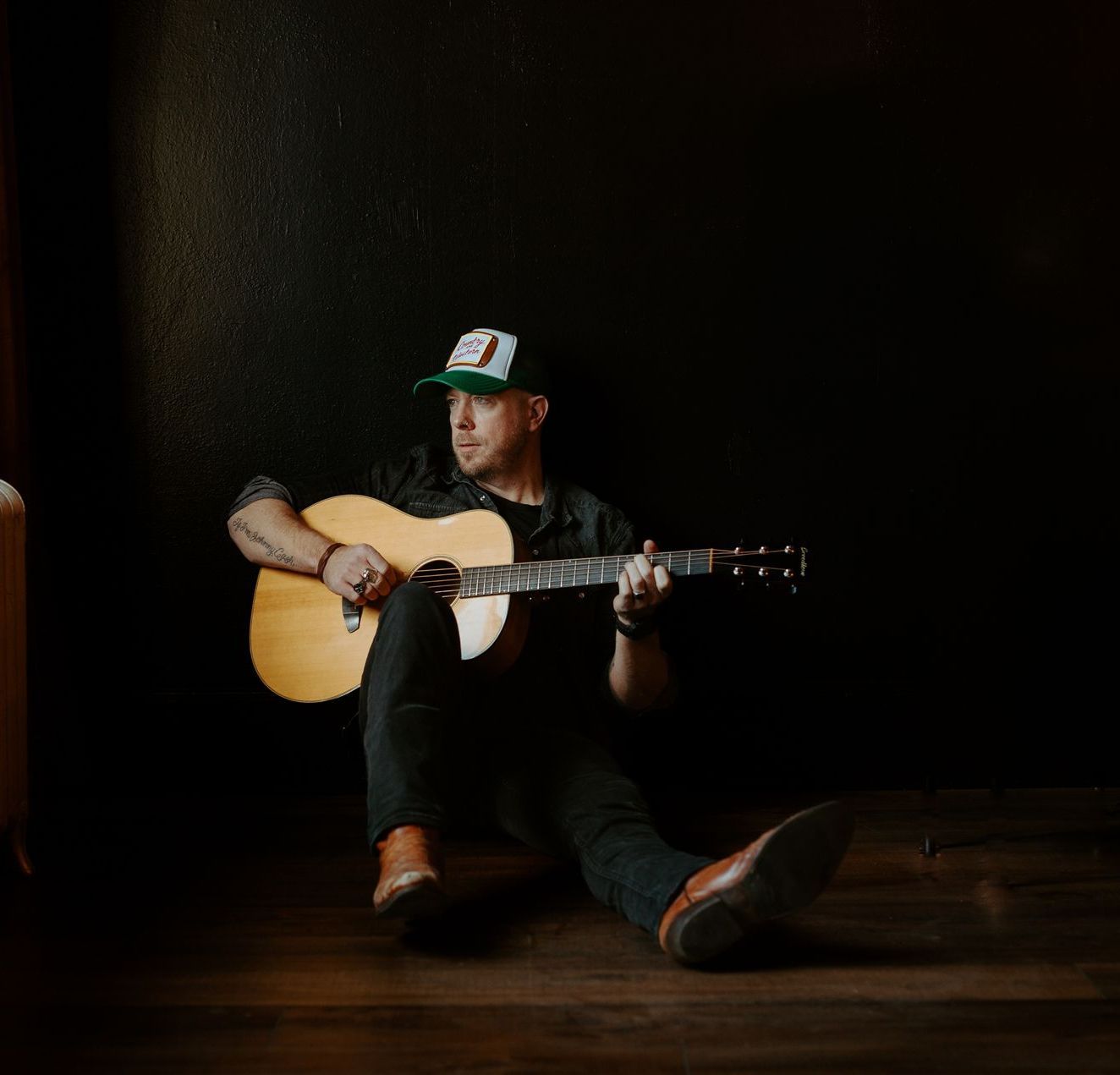 A man is sitting on the floor playing an acoustic guitar.