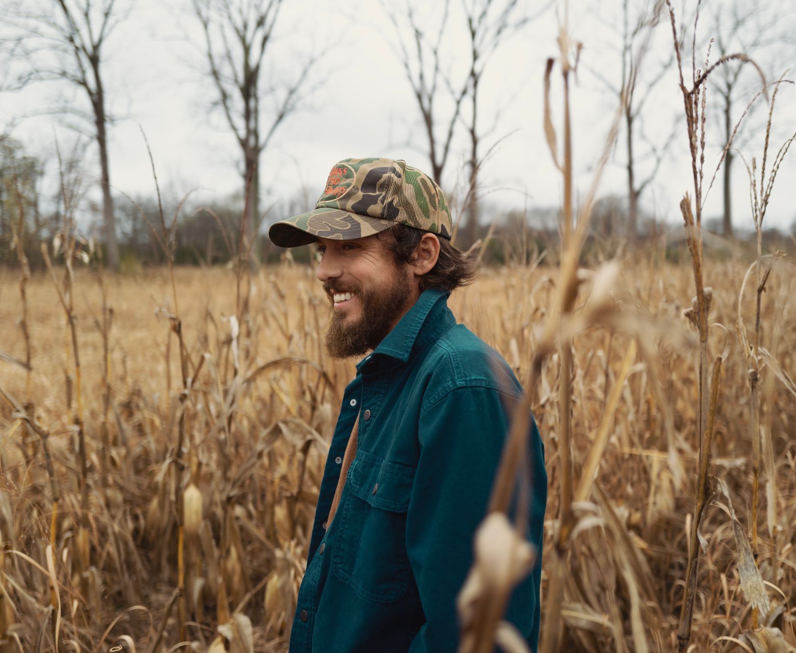 A man with a beard is standing in a field of tall grass.