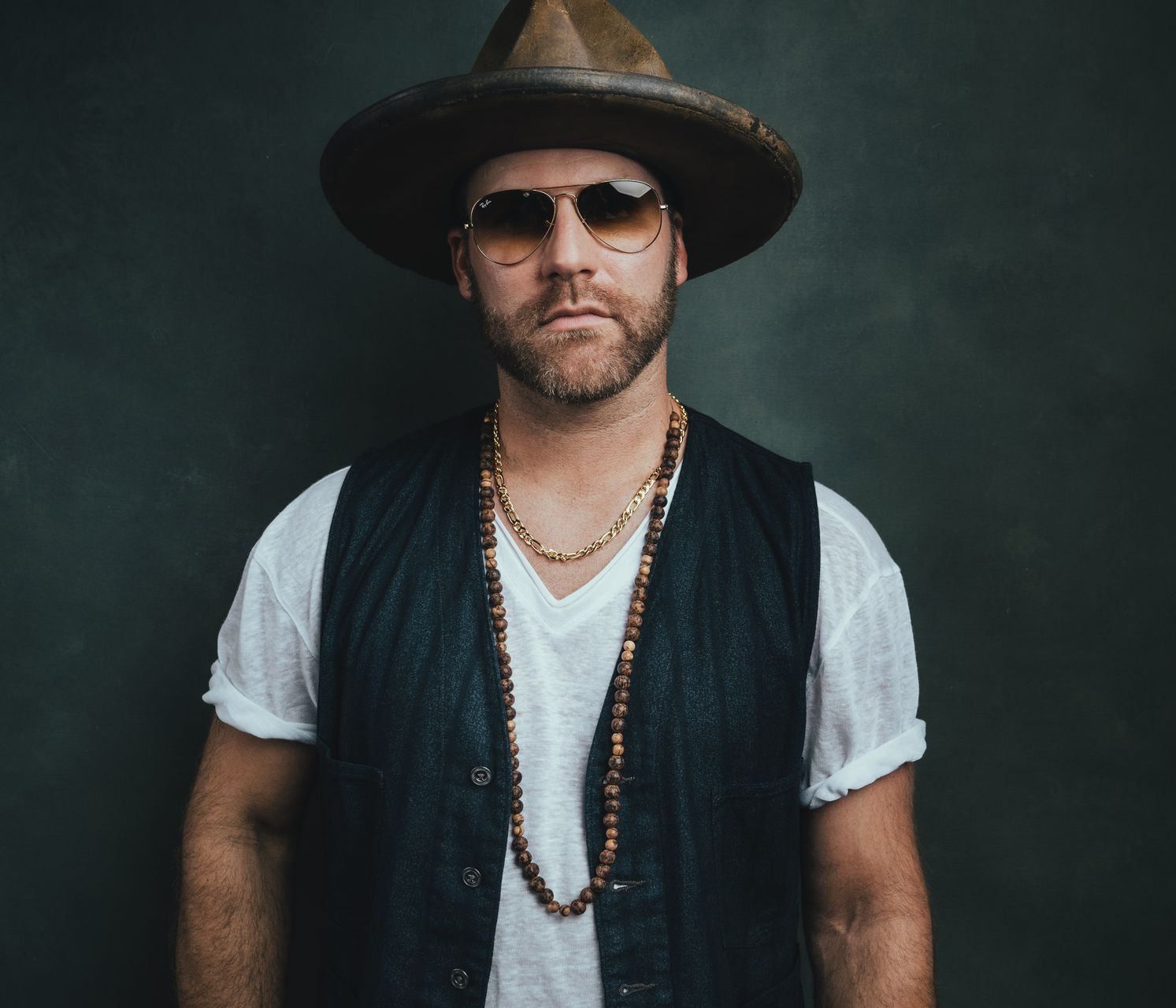 A man wearing a hat and sunglasses is standing in front of a wall.