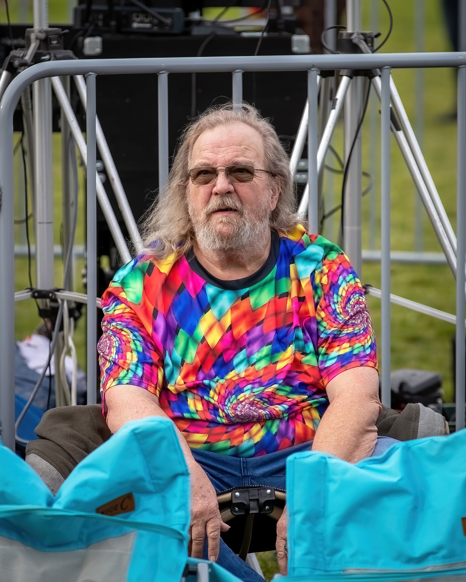 A man in a tie dye shirt is sitting in a chair.