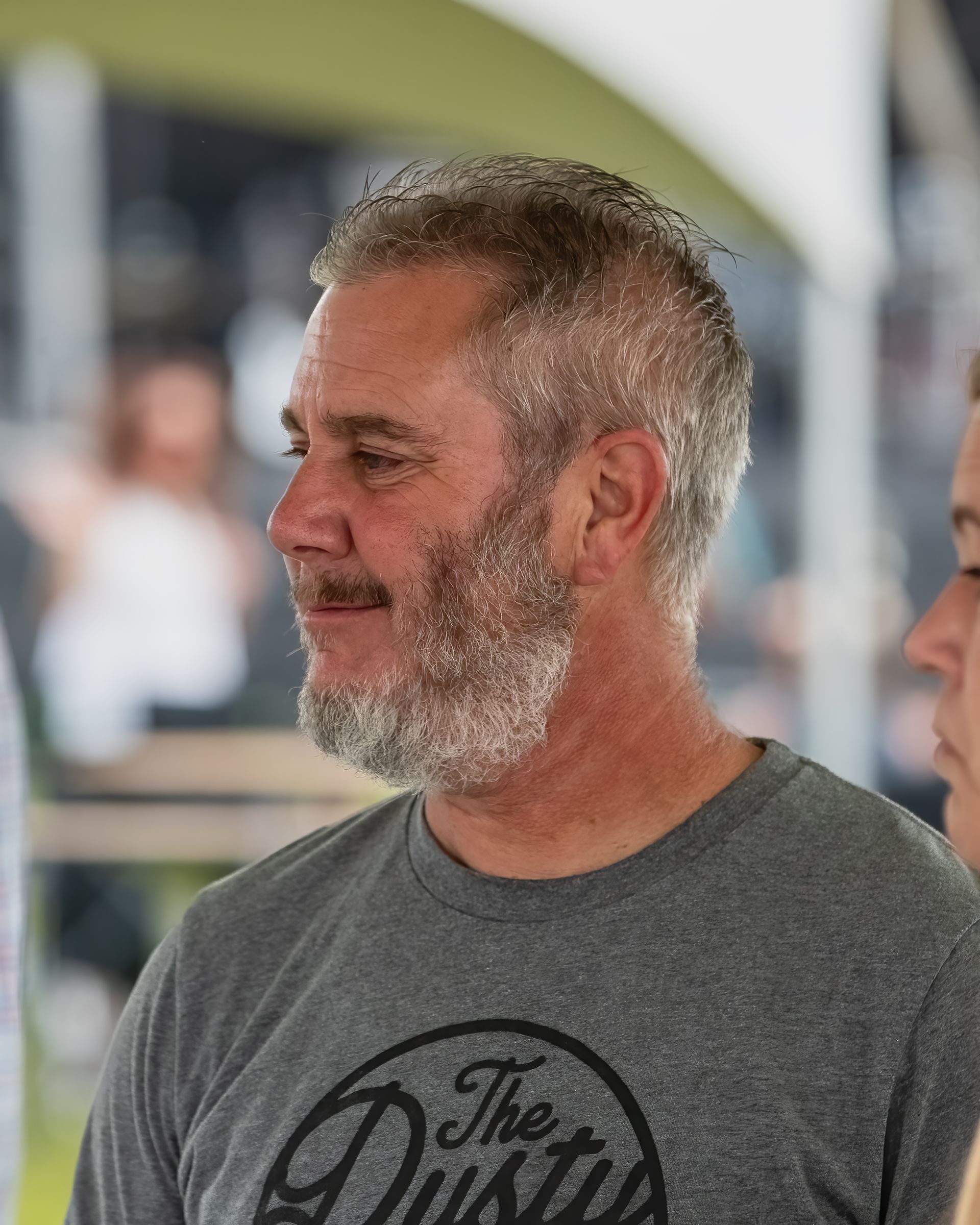 A man with a beard is wearing a grey shirt that says the dirty