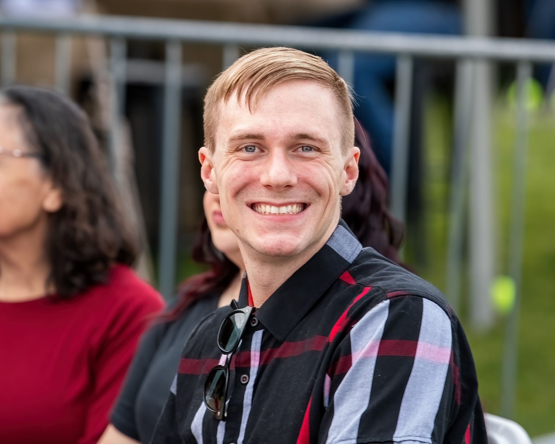 A man in a plaid shirt is smiling while sitting in a stadium.