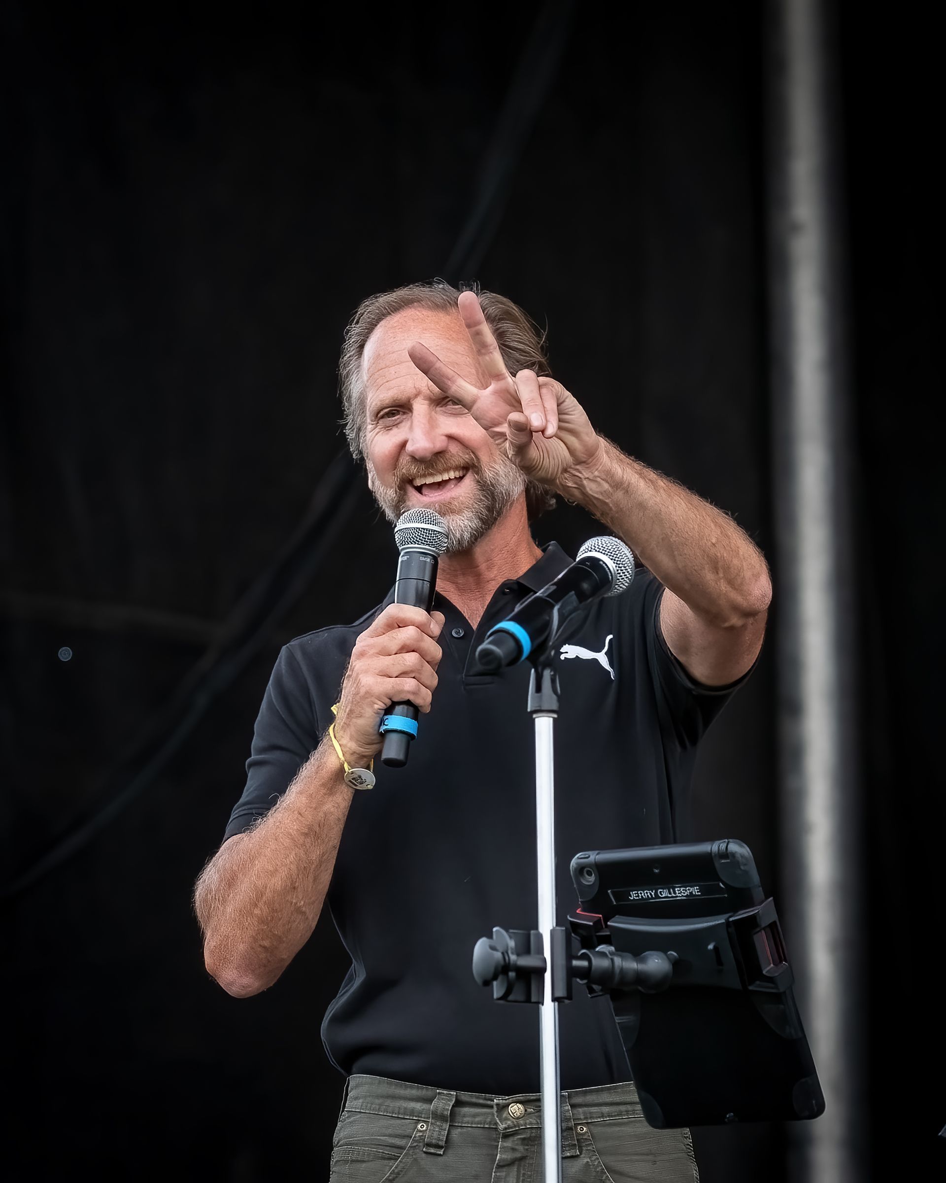 A man with a beard is holding a microphone and giving a peace sign.