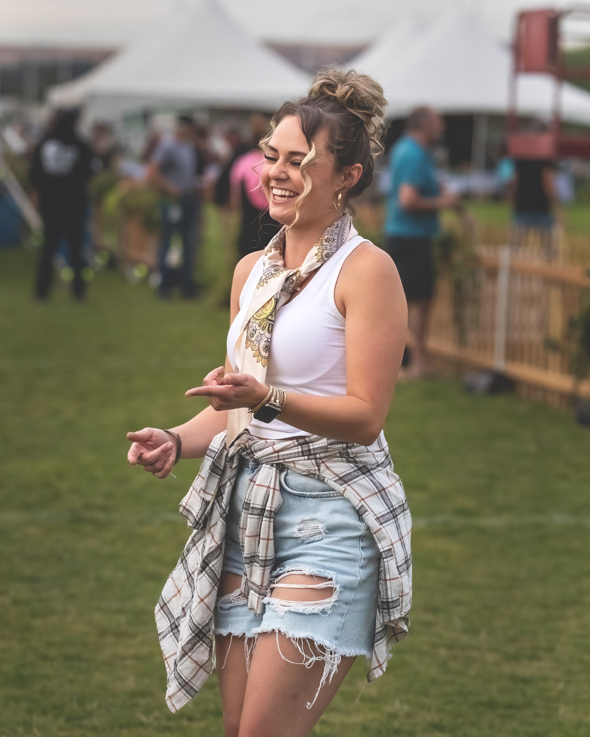 A woman in a white tank top and denim shorts is standing in a field.