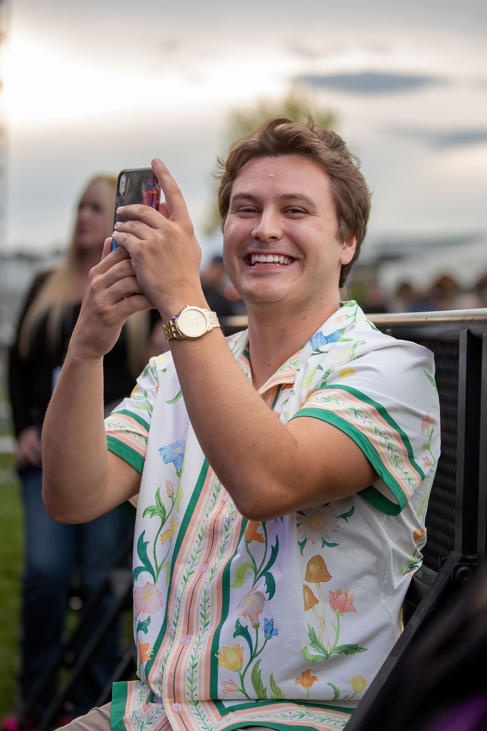A man is sitting in a chair taking a picture with his cell phone.