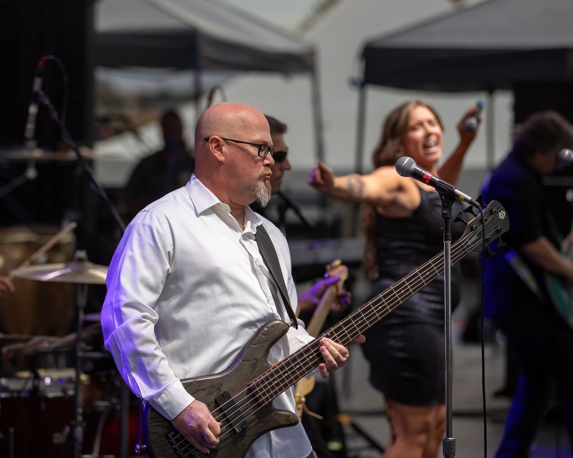A man is playing a bass guitar while a woman sings into a microphone.