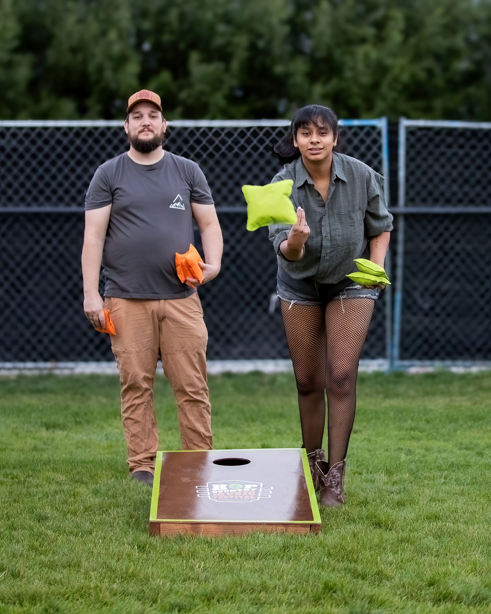 A man and a woman are playing cornhole in a field.