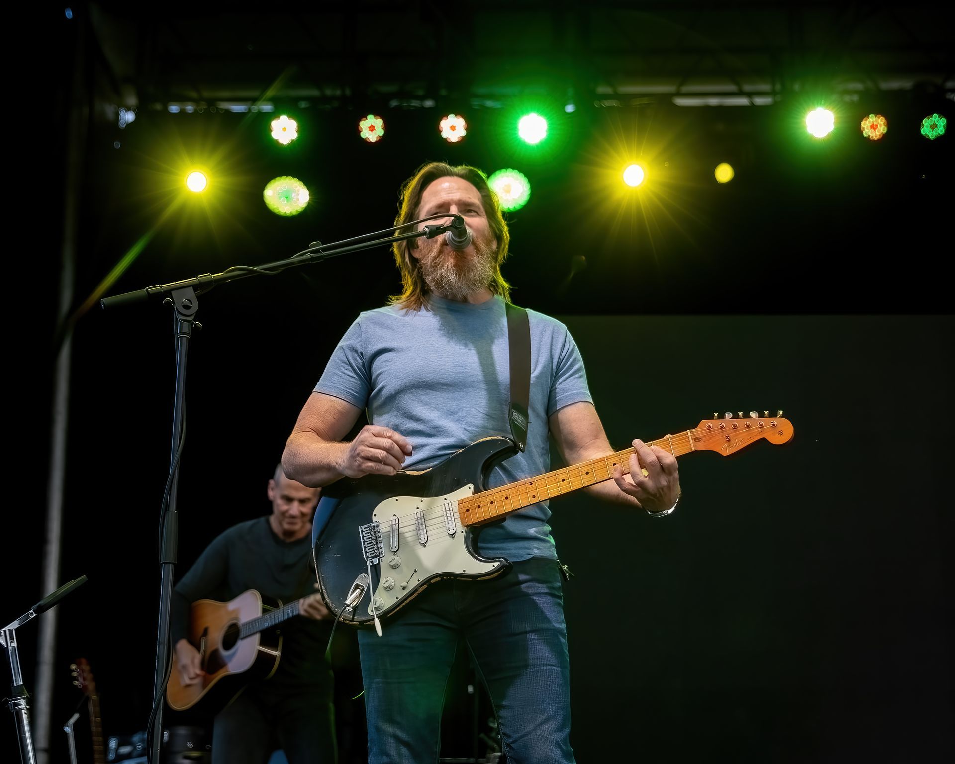 A man is playing a guitar and singing into a microphone on a stage.