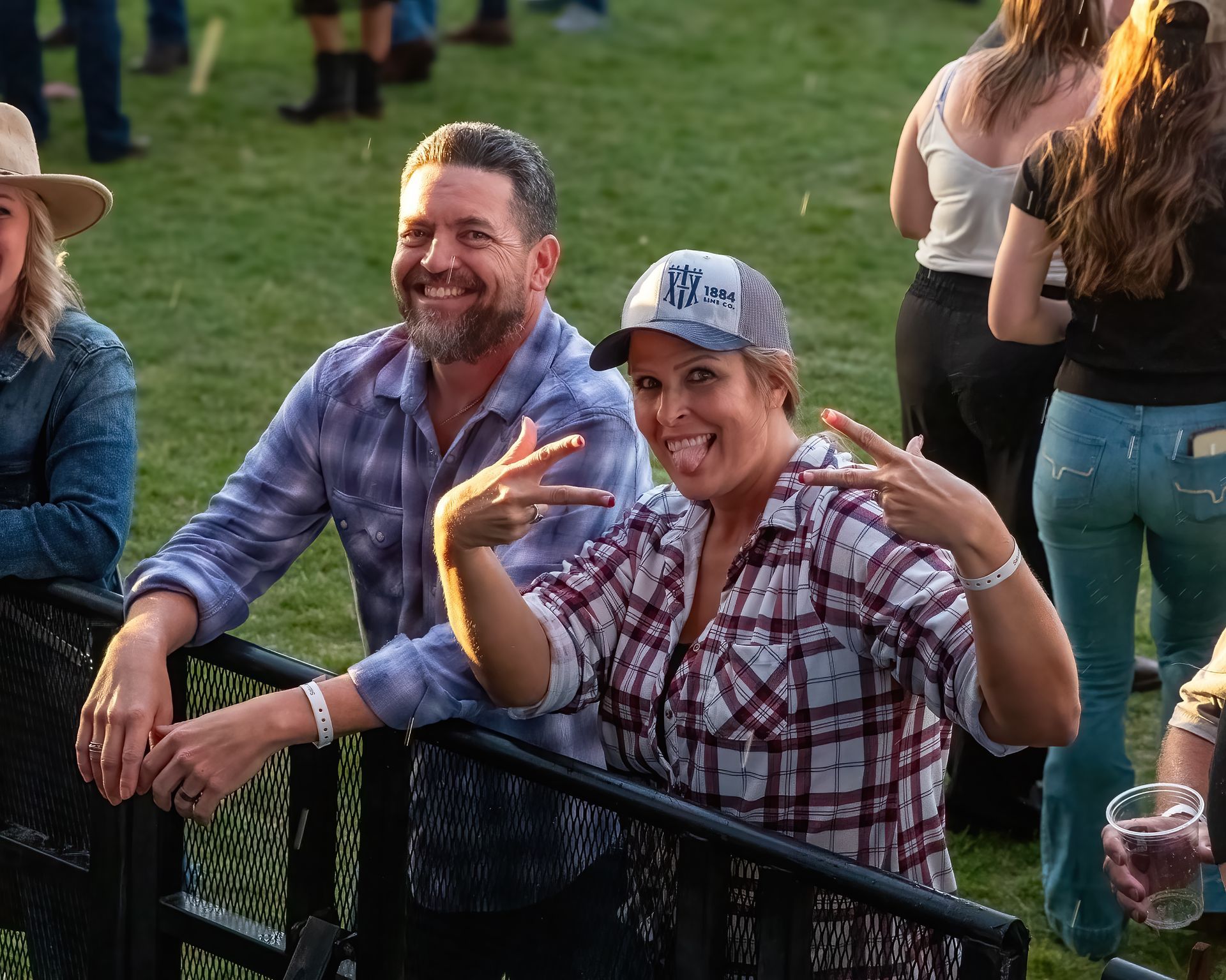 A man and a woman are posing for a picture behind a fence at a concert.