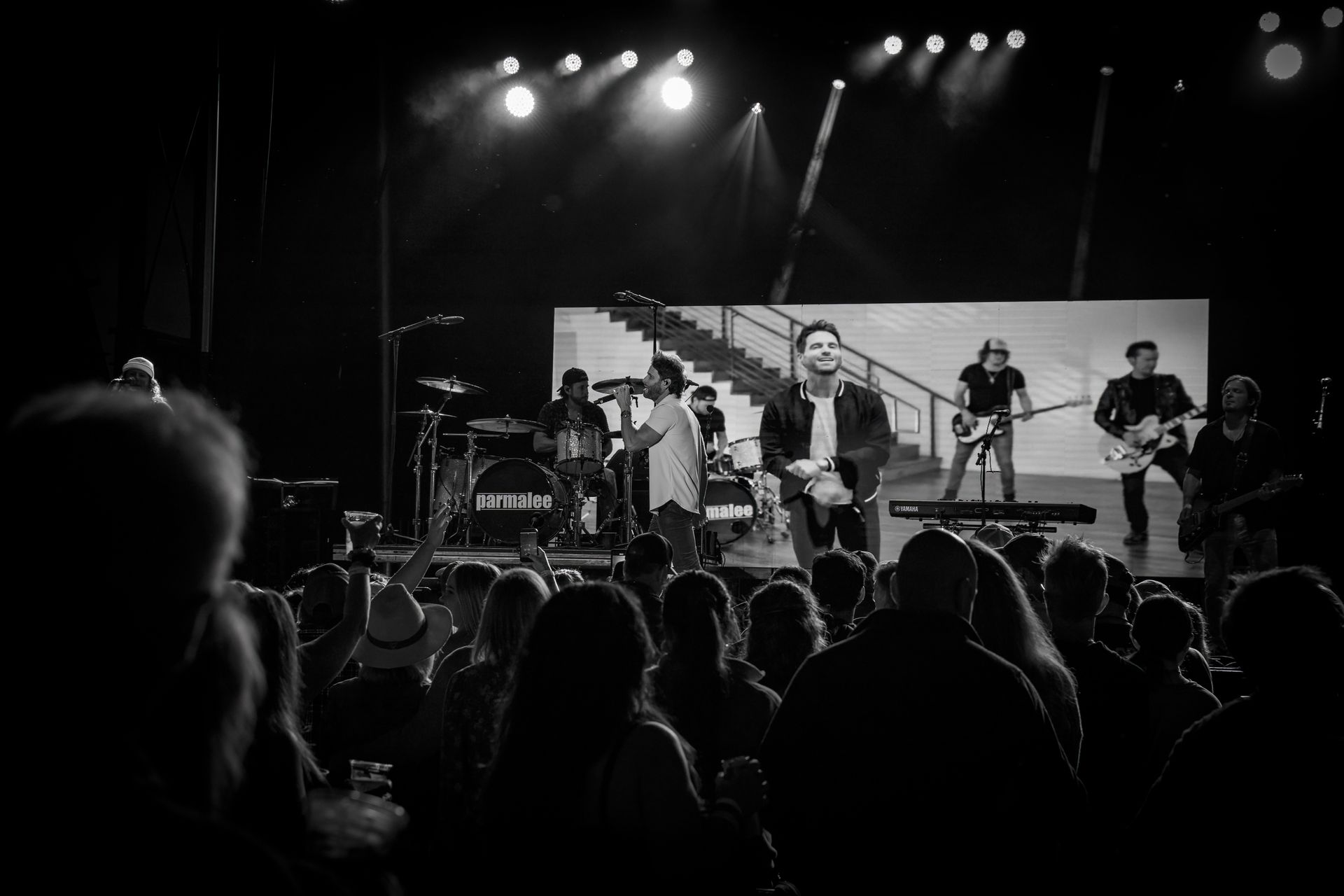 Band performing on stage with audience in front. Black and white image, bright stage lights.