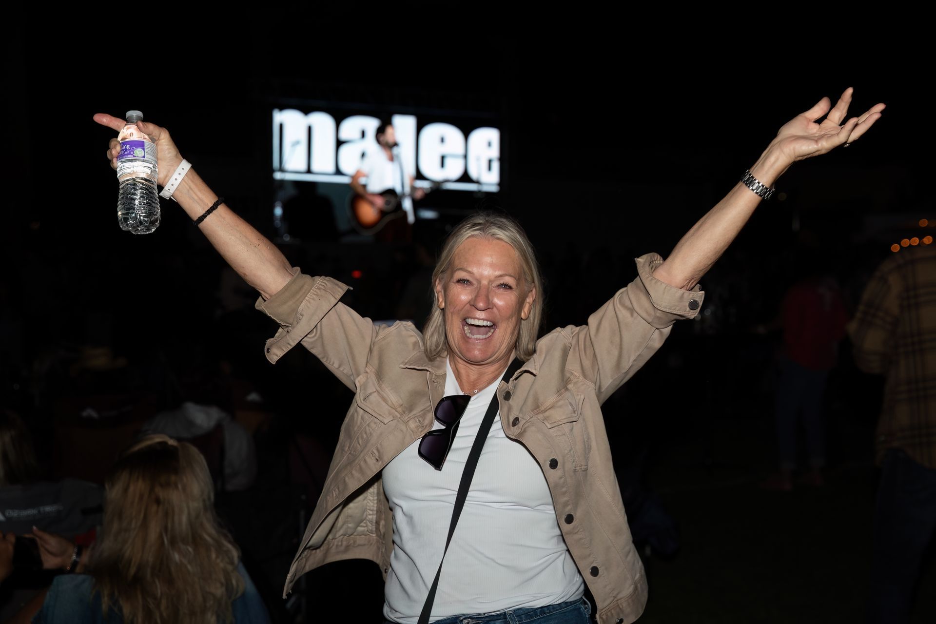 A woman is holding a bottle of water in front of a sign that says matee.