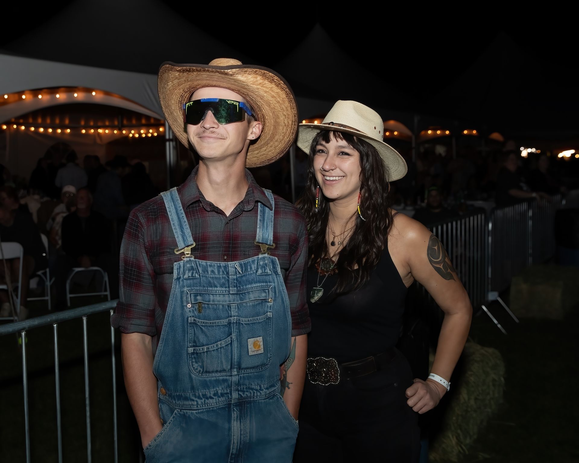 A man in overalls and a woman in a cowboy hat are posing for a picture