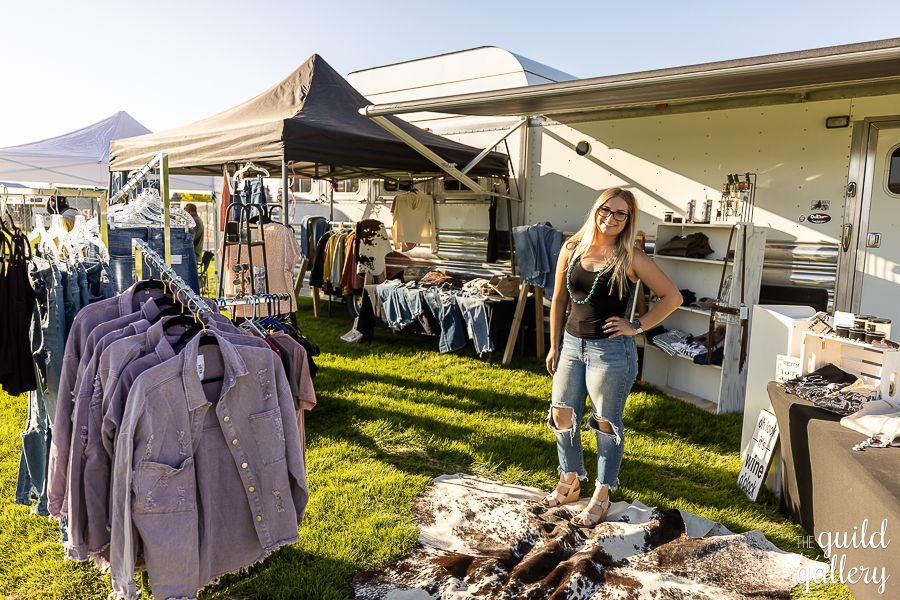 A woman is standing in front of a tent selling clothes.