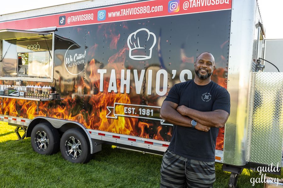 A man is standing in front of a food truck with his arms crossed.