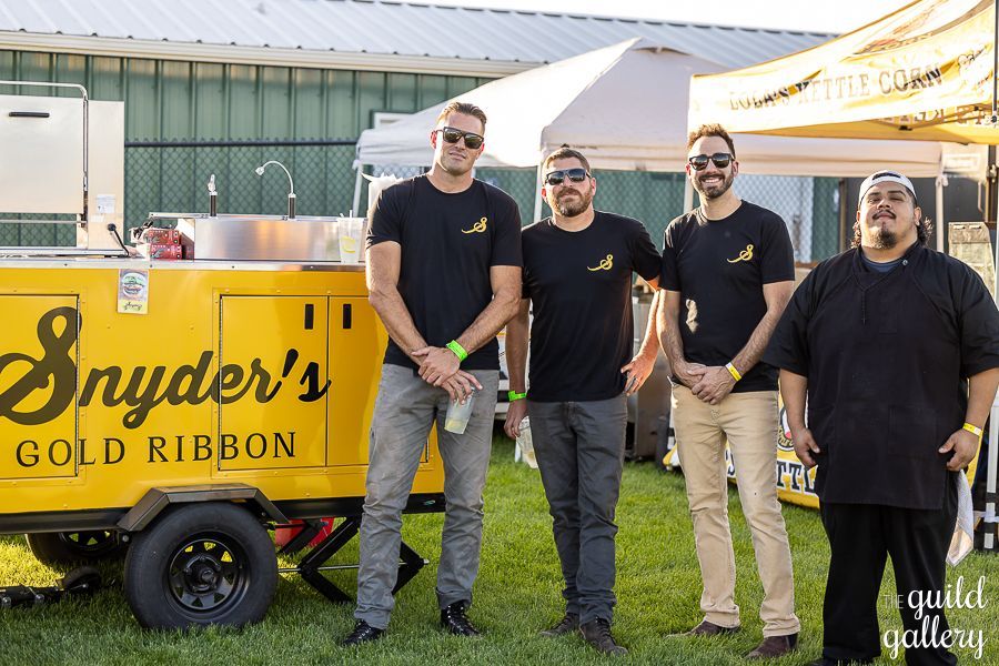 A group of men are standing in front of a yellow trailer that says snyder 's gold ribbon.