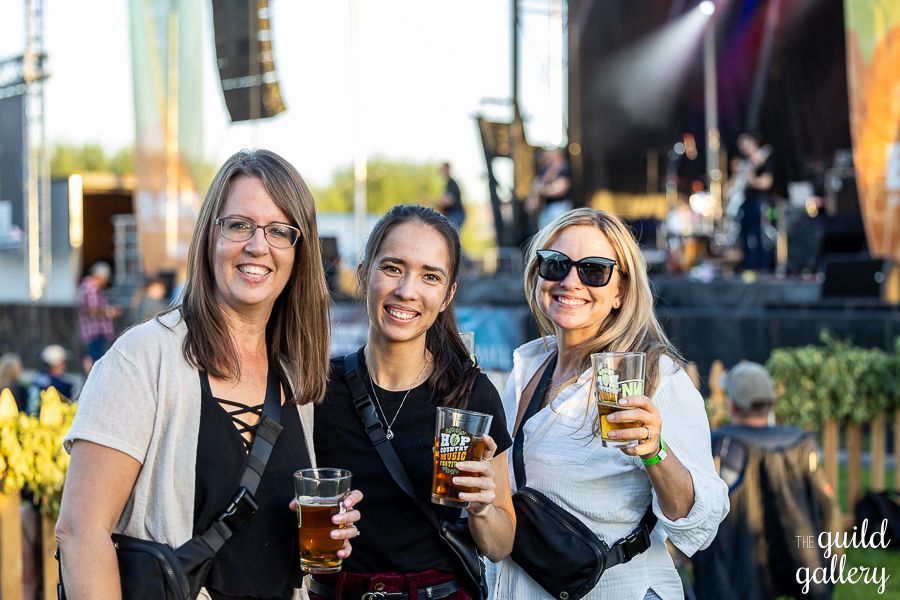 Three women are standing next to each other holding beer glasses at a concert.
