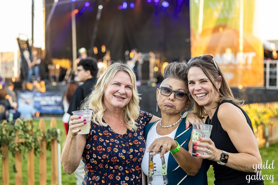 Three women are posing for a picture at a concert while holding drinks.