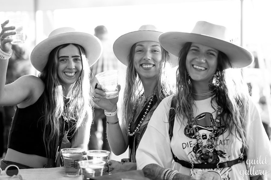 Three women wearing hats are sitting at a table holding drinks.