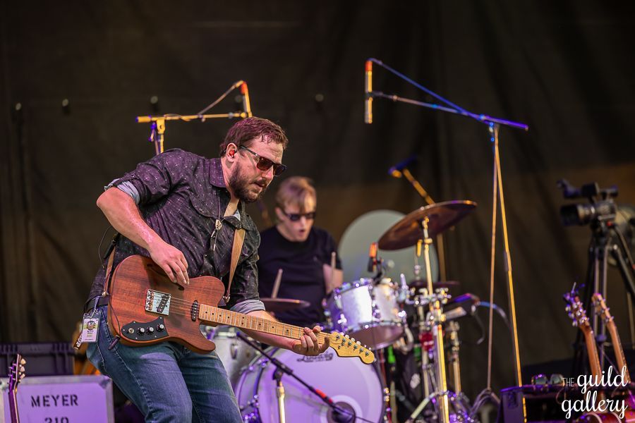 A man is playing a guitar on a stage with a drummer behind him.