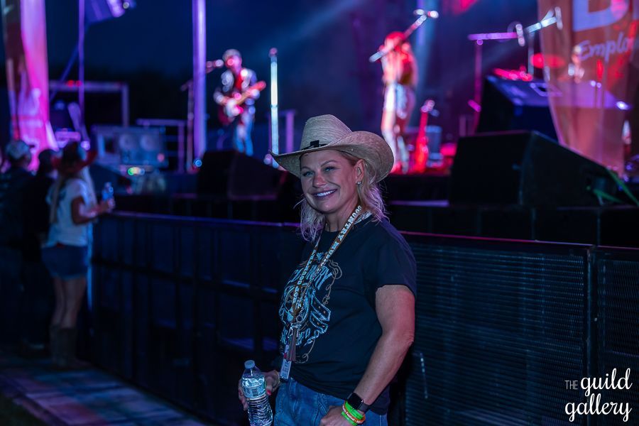 A woman in a cowboy hat is standing in front of a stage at a concert.