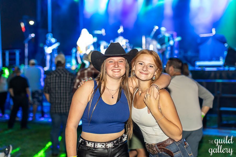 Two women are posing for a picture in front of a stage at a concert.