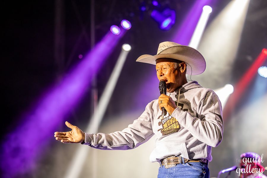 A man in a cowboy hat is holding a microphone on a stage.