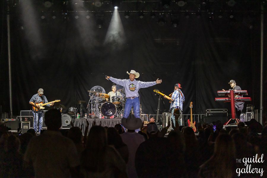 A man in a cowboy hat is standing on a stage with his arms outstretched in front of a crowd.