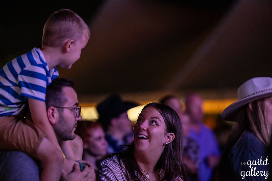 A man is holding a little boy on his shoulders at a concert.