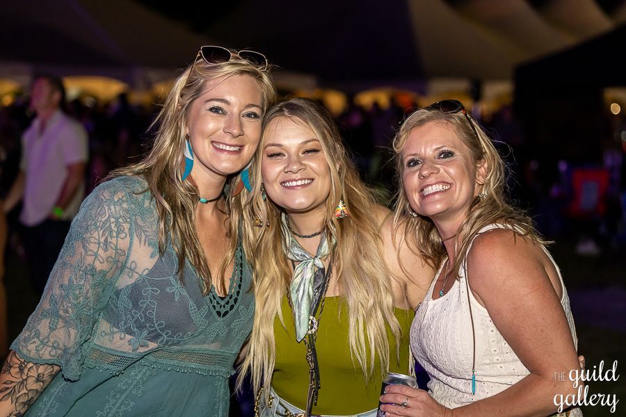 Three women are posing for a picture together at a concert.
