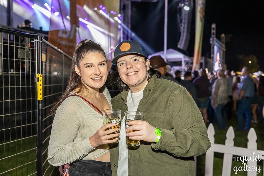 Two women are standing next to each other at a concert holding beer glasses.