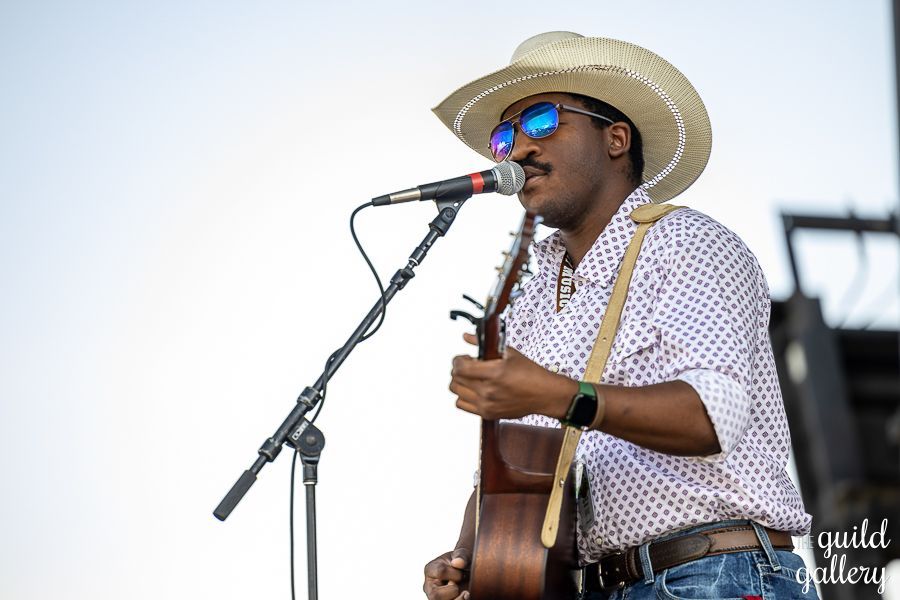 A man in a cowboy hat is singing into a microphone while playing a guitar.