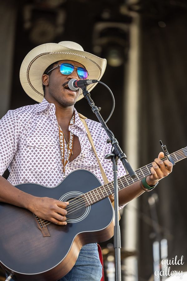 A man in a cowboy hat is playing a guitar and singing into a microphone.