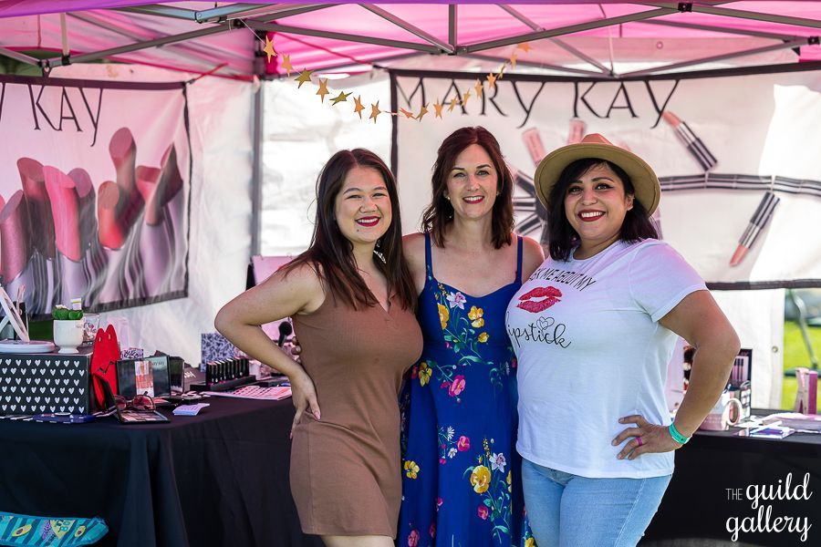 Three women are posing for a picture in front of a mary kay tent.