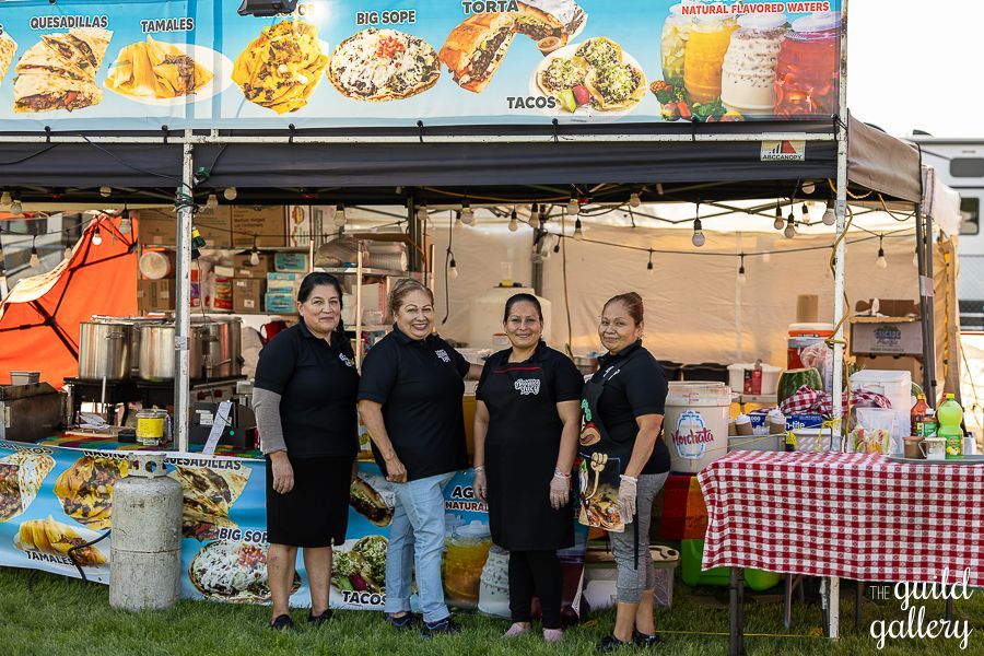 A group of women are standing in front of a food stand.