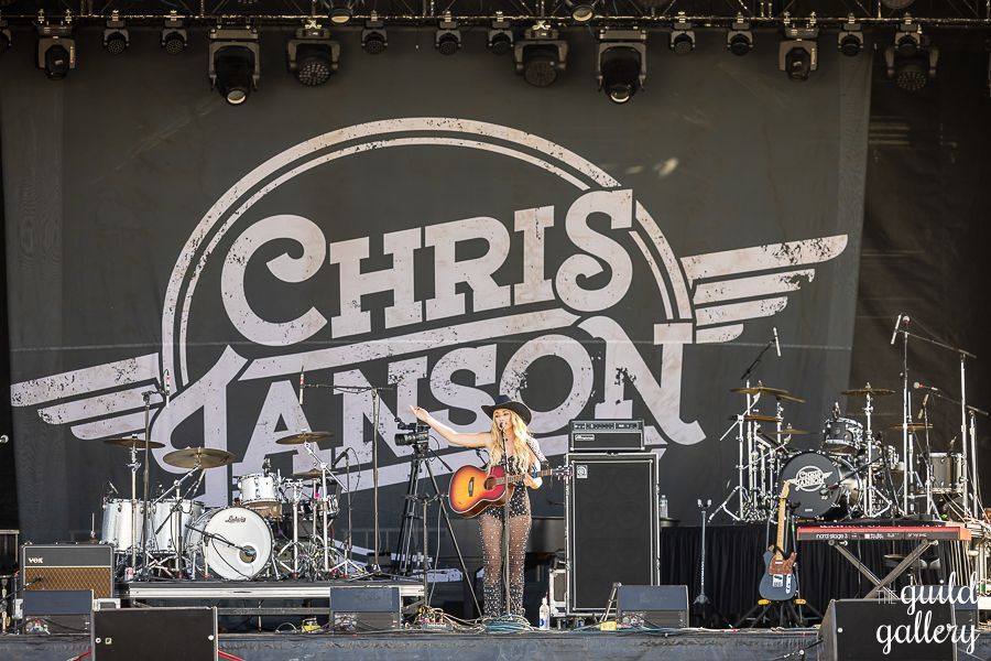 A woman is playing a guitar on a stage in front of a large chris manson logo.