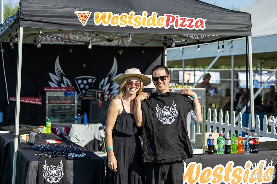 A man and a woman are standing in front of a westside pizza tent.